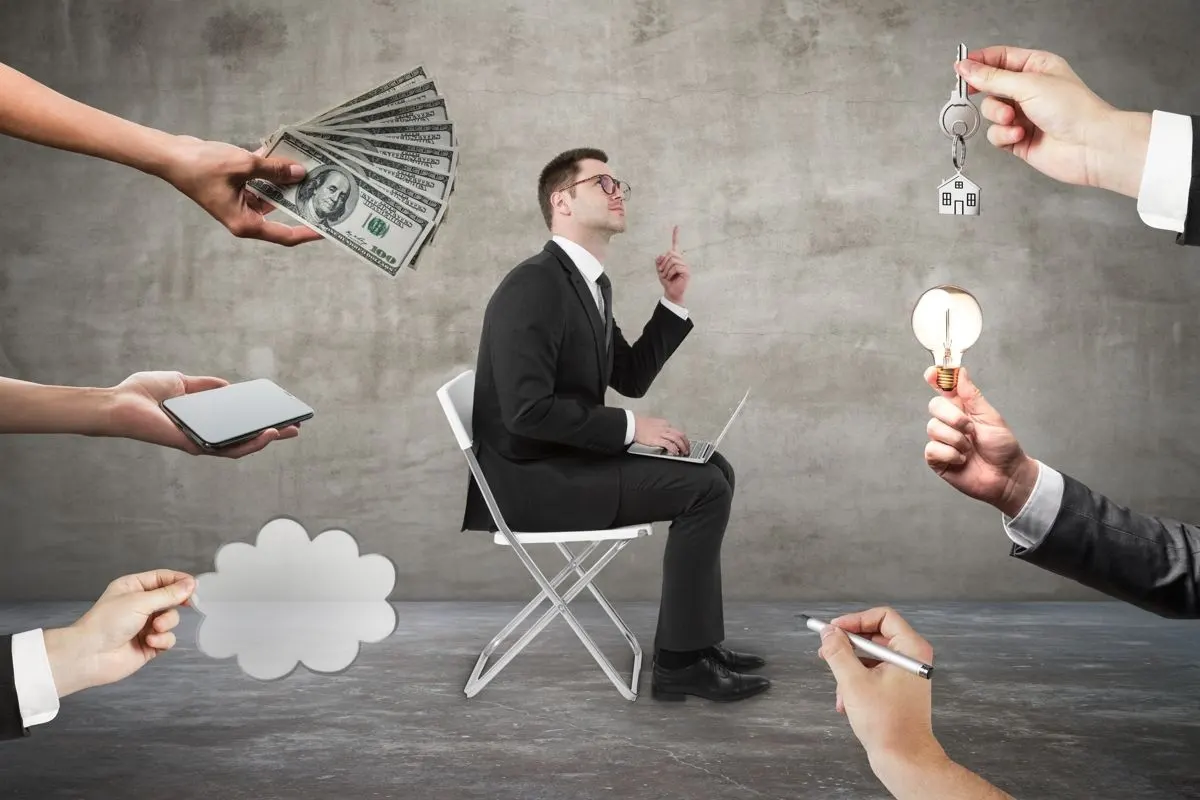 A man in a chair with hands extended towards him holding money, a pen, a lightbulb and other objects